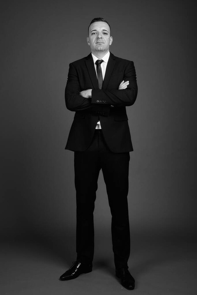 Studioaufnahme eines Geschäftsmannes im Anzug vor grauem Hintergrund in Schwarz-Weiß - Foto, Bild