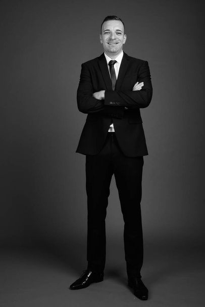 Στούντιο πλάνο του επιχειρηματία φορώντας κοστούμι σε γκρι φόντο σε μαύρο και άσπρο - Φωτογραφία, εικόνα