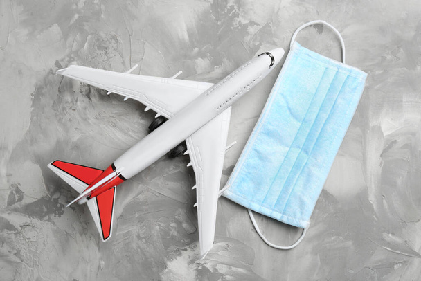 Toy airplane and protective mask on grey background, flat lay. Travelling during coronavirus pandemic - Foto, imagen