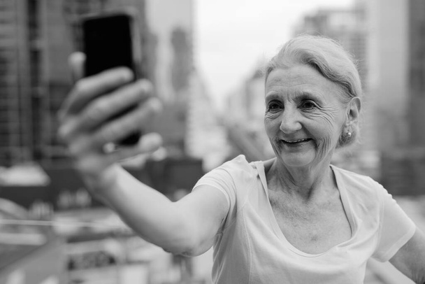 Портрет красивої старшої жінки з світлим волоссям на тлі вигляду міста в чорно-білому
 - Фото, зображення
