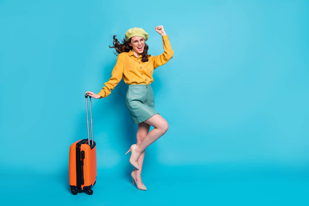 Full size photo of ecstatic girl win weekend lottery tour raise fists scream hold suitcase wear style stylish trendy yellow blouse stilettos isolated over blue color background - Foto, Bild