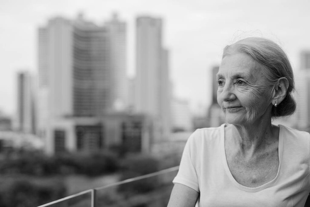 Retrato de una hermosa mujer mayor con el pelo rubio contra la vista de la ciudad en blanco y negro - Foto, imagen