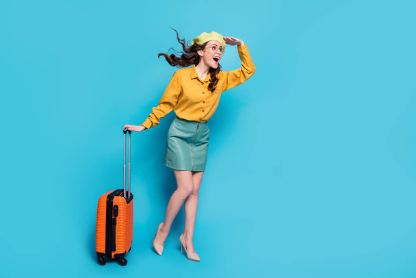 Full length photo excited girl tourist hold hand head see plane wavy haircut fly blow hold baggage wear yellow blouse style stylish trendy stilettos isolated over blue color background - Fotografie, Obrázek