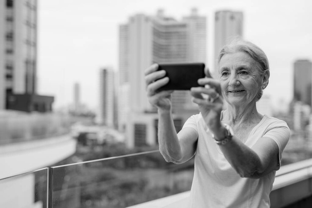 Retrato de una hermosa mujer mayor con el pelo rubio contra la vista de la ciudad en blanco y negro - Foto, imagen
