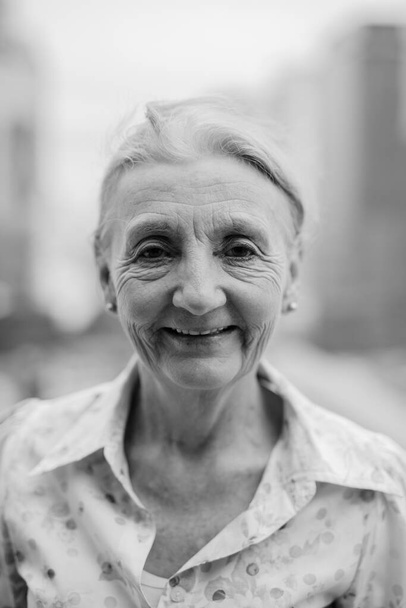 Портрет красивої старшої жінки з світлим волоссям на тлі вигляду міста в чорно-білому
 - Фото, зображення