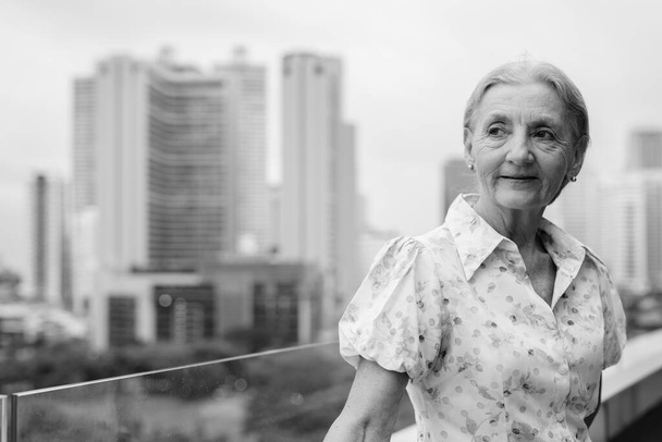 Портрет красивой пожилой женщины с светлыми волосами с видом на город в черно-белом цвете - Фото, изображение