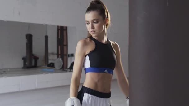 Retrato de uma jovem boxeadora atraente no ginásio usando luvas ao lado de um saco de perfuração - Filmagem, Vídeo