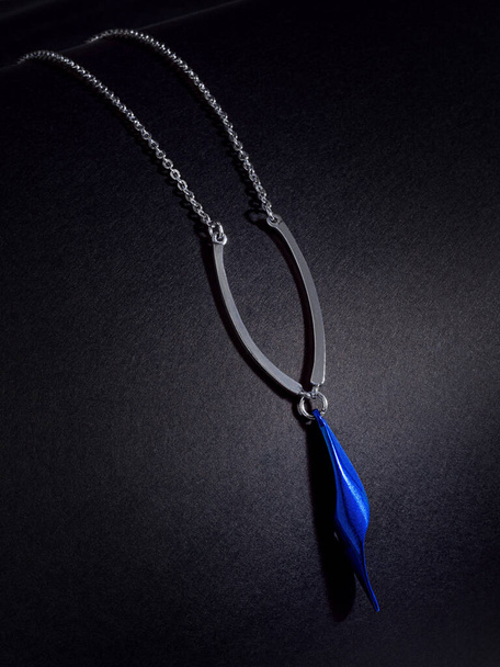 collar de cadena delgada con joya azul sobre fondo negro con textura de papel - Foto, Imagen