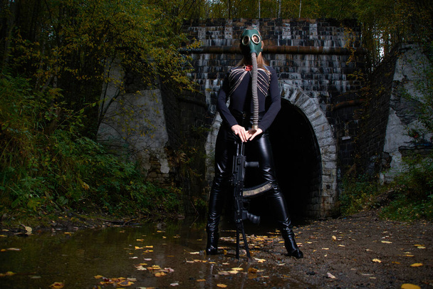 una mujer en traje negro y máscara de gas con una ametralladora en las manos. - Foto, Imagen