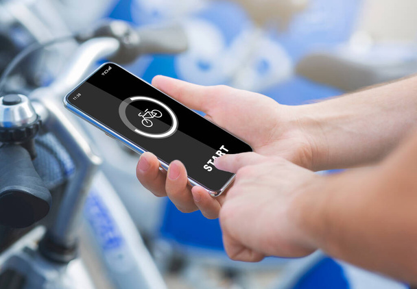 Smart bicycle travel, gadgets and activity control. Male hands press start of button on smartphone - Photo, Image