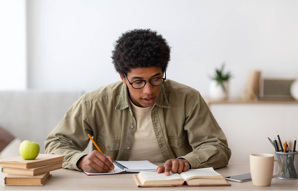 Uczenie się na odległość. czarny nastolatek college student z podręcznik i copybook studiuje w domu podczas zamknięcie - Zdjęcie, obraz
