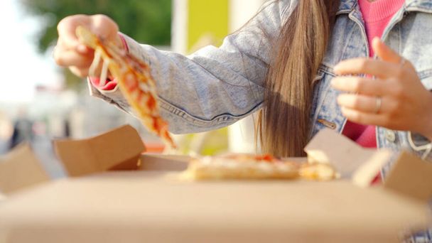 Włoskie jedzenie, kobieta jedząca pizzę z mozzarellą na świeżym powietrzu. Media. Zbliżenie młodej kobiecej dłoni biorącej kawałek pizzy w letni słoneczny dzień. - Zdjęcie, obraz