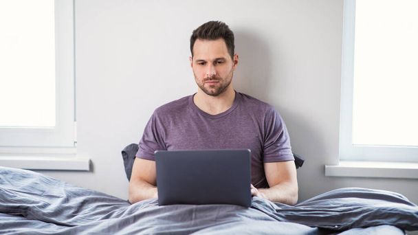 Homem Freelancer Trabalhando no Laptop Online Sentado na cama Interior - Foto, Imagem