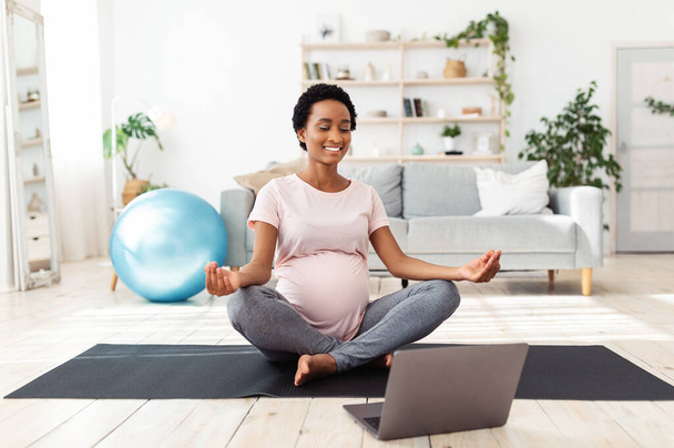 Beautiful pregnant woman meditating to online video on laptop computer at home - Foto, Imagen