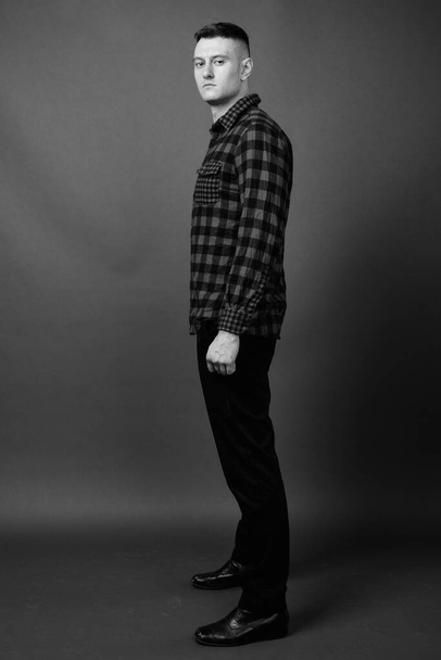 Studio shot of young handsome man wearing checkered shirt against gray background in black and white - Photo, Image