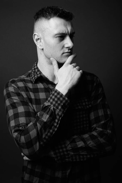 Studio shot of young handsome man wearing checkered shirt against gray background in black and white - Фото, изображение
