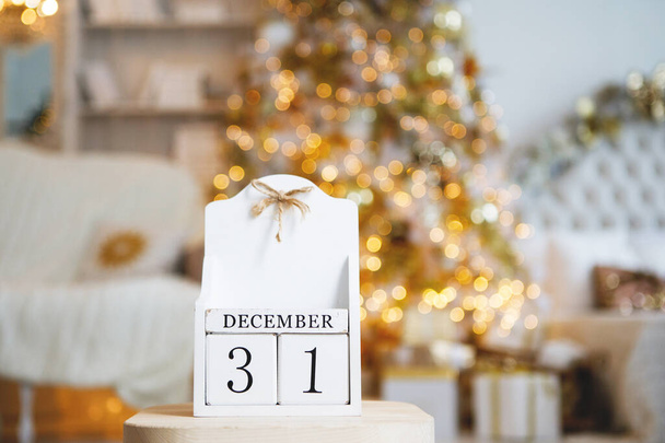 Old vintage calendar of wooden cubes with the date of December 31 on the background of a Christmas tree with burning blurry lights. Selected focus in the foreground. - Photo, Image