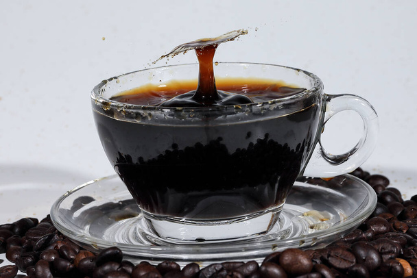 Filar splash kawy w przezroczystym szklanym talerzu filiżanka pełna płynnej kawy na kawie został biały tło łóżko - Zdjęcie, obraz
