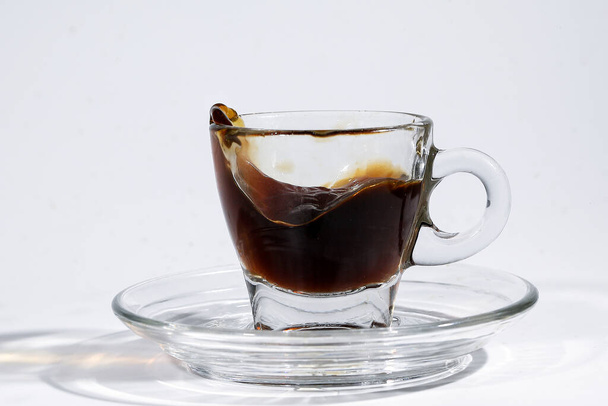 Koffie splash golf in transparant glas espresso kopje schotel vol met vloeibare koffie op witte achtergrond - Foto, afbeelding