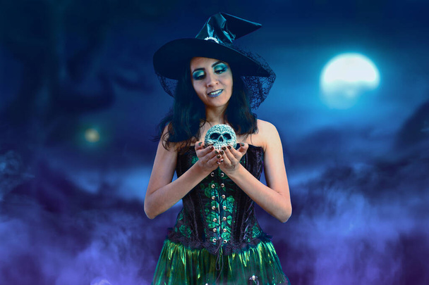 Fiatal boszorkány gyönyörű zöld ruha és ijesztő koponya halloween éjszaka. - Fotó, kép