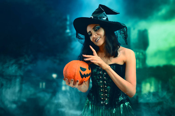 Beautiful witch with a pumpkin in halloween night. - Fotoğraf, Görsel