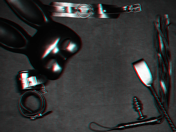 набор секс-игрушек на черном фоне. Кожаный кнут, наручники, удушитель, маска и металлическая анальная пробка для БДСМ секса и ролевых игр - Фото, изображение