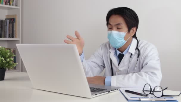 Young Asian Doctor Man in Lab Coat or Gown with Stethoscope Wear Face Mask Exam Patient by Video Conference or Video Chat in Office - Footage, Video