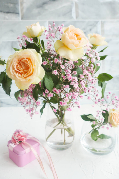 μπουκέτο από ροδακινί σπρέι τριαντάφυλλα και γυψόφυλλες και ροζ κουτί δώρου σε λευκό τραπέζι - Φωτογραφία, εικόνα