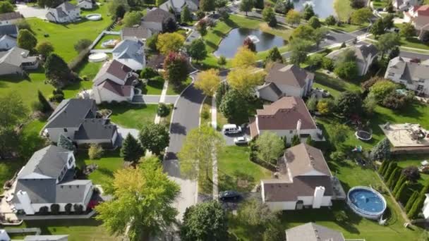 Vista aérea aérea de árvores coloridas de outono, casas residenciais e quintais com lagoa de drenagem ao longo da rua suburbana na área de Chicago. Centro-Oeste dos EUA - Filmagem, Vídeo