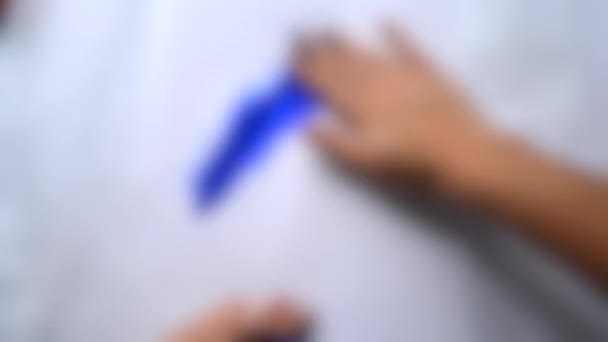 Wazige achtergrond. Meisje handen verf blauwe verf op het witte papier. - Video