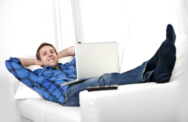 Hombre atractivo con el ordenador sentado en el sofá
 - Foto, imagen