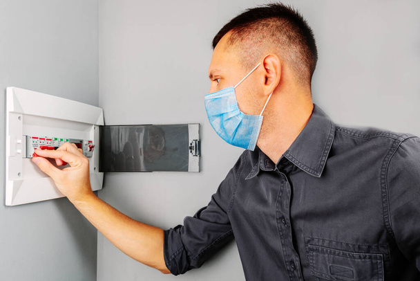 an electrician repairing a mask switch during a pandemic covid - 19. Hands of electrician with electric actuator equipment in fuse box - Fotoğraf, Görsel