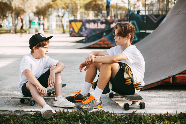 Двоє найкращих друзів у парку скейтбордів. Друзі сидять на ковзанах у парку, розмовляють і посміхаються. Друзі, дружба, активний відпочинок
 - Фото, зображення