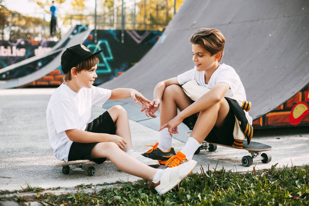 Due migliori amici in uno skateboard Park. Gli amici si siedono sui pattini nel parco, parlando e sorridendo. Amici, amicizia, attività all'aria aperta - Foto, immagini