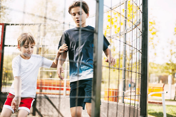 Dos adolescentes lindos juegan al fútbol en el campo de fútbol de estilo libre. Los chicos pelean por la pelota en el juego. Deporte, juego, competición, fútbol libre - Foto, Imagen