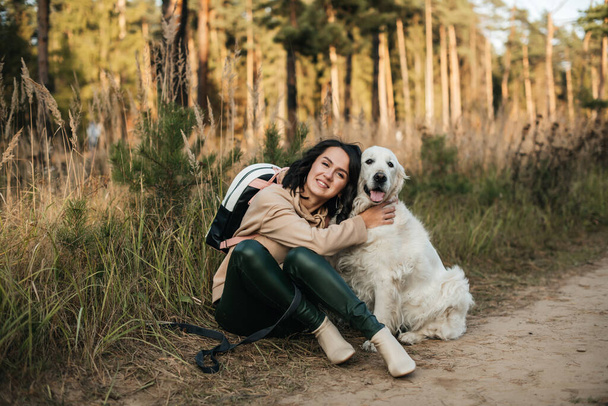 brunette girl sitting with white golden retriever dog on the forest path - Φωτογραφία, εικόνα