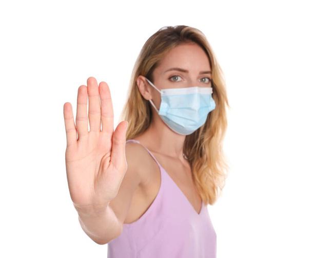 Woman in protective face mask showing stop gesture on white background, focus on hand. Prevent spreading of coronavirus - Foto, Bild