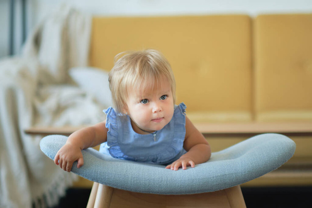 Küçük mavi gözlü kız sandalyeye tutunarak yürümeyi öğreniyor. Mutlu bebek yüzü - Fotoğraf, Görsel