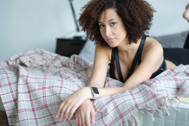 pretty woman with a curly hair on a bed. portrait young smiling black woman - 写真・画像