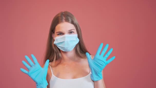 医療用マスクをした若い女性がカメラを見てラテックス手袋と親指を手に - 映像、動画