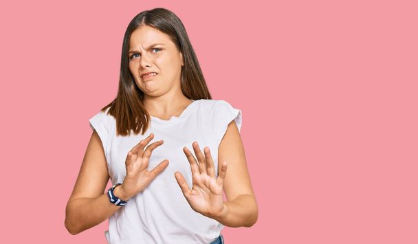 Young caucasian woman wearing casual white tshirt disgusted expression, displeased and fearful doing disgust face because aversion reaction. with hands raised  - Photo, Image