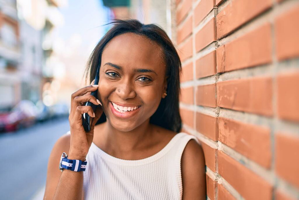 Jeune femme afro-américaine souriante heureuse de parler sur le smartphone de la ville. - Photo, image
