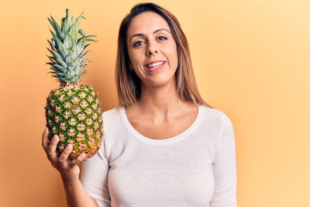 Young beautiful woman holding pineapple looking positive and happy standing and smiling with a confident smile showing teeth  - Photo, Image