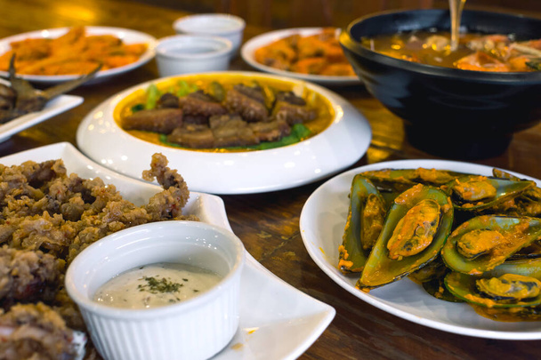 Een assortiment Filipijnse gerechten op een houten tafel in een lokaal restaurant. Inbegrepen zijn onder andere Calamares en Mosselen. - Foto, afbeelding
