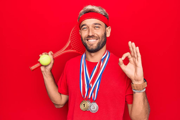 Handsome blond sportsman with beard winning medals playing tennis using racket and ball doing ok sign with fingers, smiling friendly gesturing excellent symbol - Photo, Image