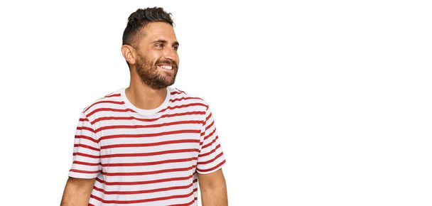 Handsome man with beard wearing striped tshirt looking away to side with smile on face, natural expression. laughing confident.  - Photo, Image