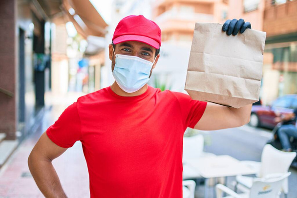 Jeune accoucheur portant un uniforme et un masque médical de protection contre le coronavirus. Tenant emporter sac en papier à la rue de la ville. - Photo, image