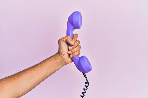 Hispanic hand holding vintage telephone over isolated pink background. - Foto, imagen