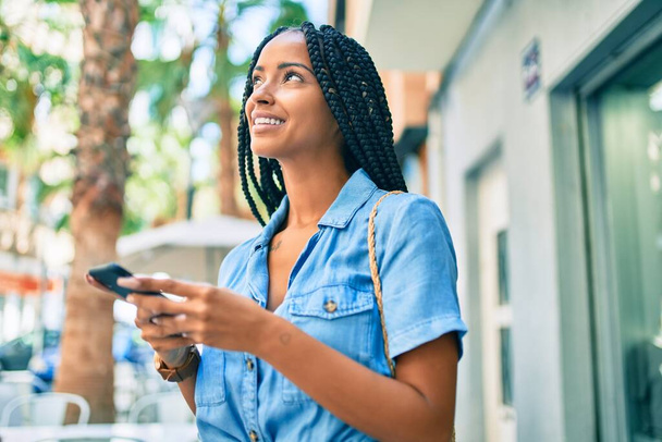 Fiatal afro-amerikai nő mosolyog boldog segítségével smartphone a városban. - Fotó, kép