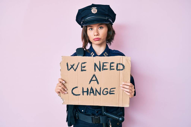 Молодая красивая женщина в полицейской форме проведение нам нужно изменение баннер мышления отношение и трезвое выражение лица глядя уверенно  - Фото, изображение